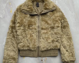May include: A tan faux fur jacket featuring a high collar, a full-length front zipper, and ribbed elastic cuffs and hem. The jacket is constructed with a plush, textured synthetic fur exterior and a smooth, matching tan interior lining.