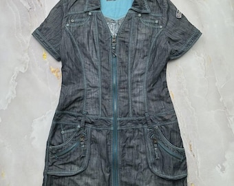 Puede incluir: Un vestido de mezclilla gris oscuro con cremallera frontal completa, mangas cortas y cuello. La prenda incluye dos bolsillos delanteros grandes con cierre de cremallera, costuras decorativas y un forro interior azul brillante en el cuello.