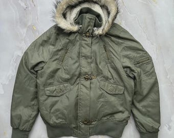 May include: An olive green bomber jacket featuring a hood with a faux fur trim, ribbed cuffs and hem, two chest zipper pockets, two lower flap pockets with snap buttons, and three metal toggle closures down the center front of the garment.