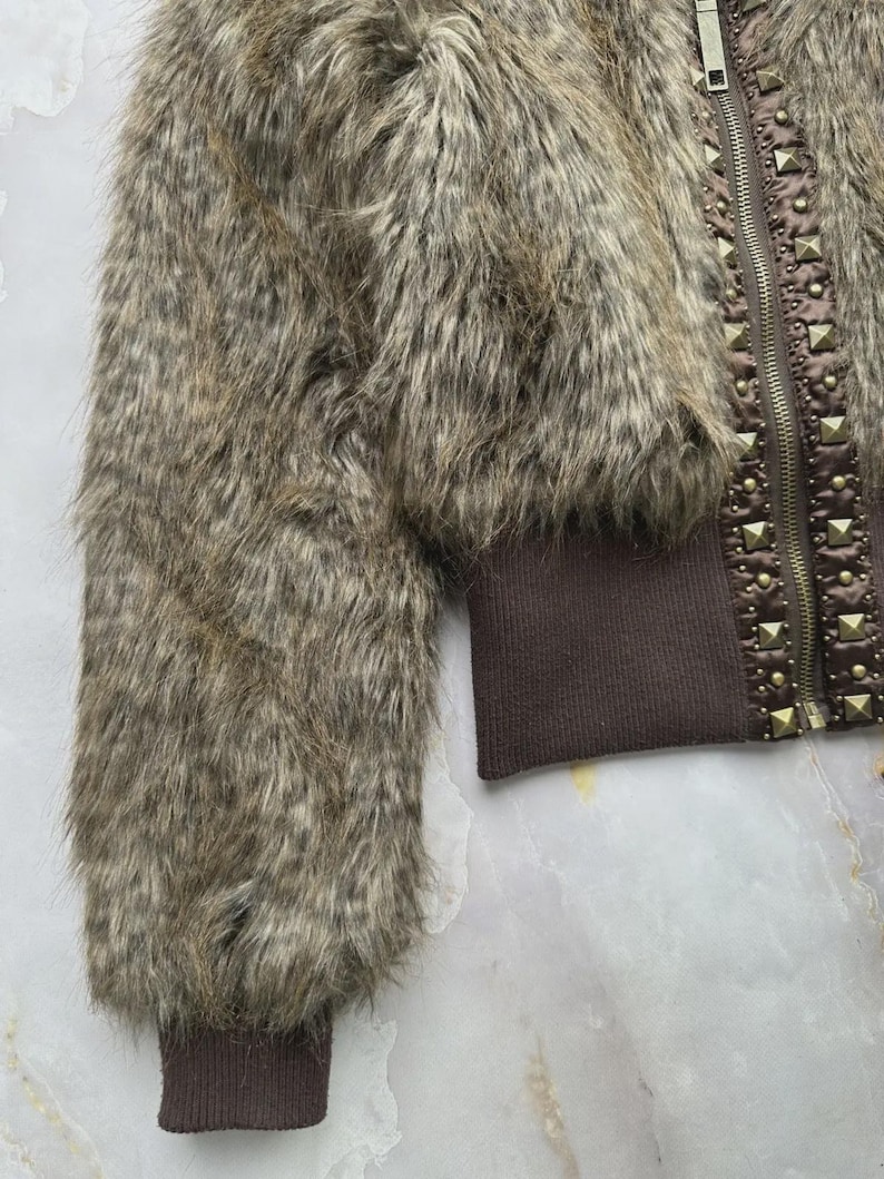 Puede incluir: Chaqueta de piel sint&eacute;tica marr&oacute;n con cierre de cremallera y detalles de tachuelas. La chaqueta tiene mangas largas con pu&ntilde;os de canal&eacute;. La piel es una mezcla de tonos marrones y grises.