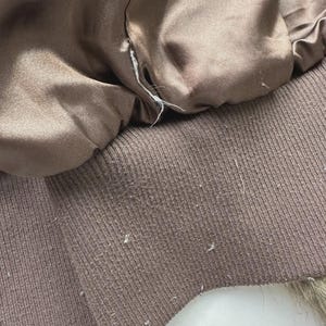 Puede incluir: Primer plano del forro de una chaqueta marr&oacute;n. El forro es de un material liso, similar al sat&eacute;n, y el pu&ntilde;o es de punto acanalado. La costura es visible donde el forro se encuentra con el pu&ntilde;o. La chaqueta parece usada.