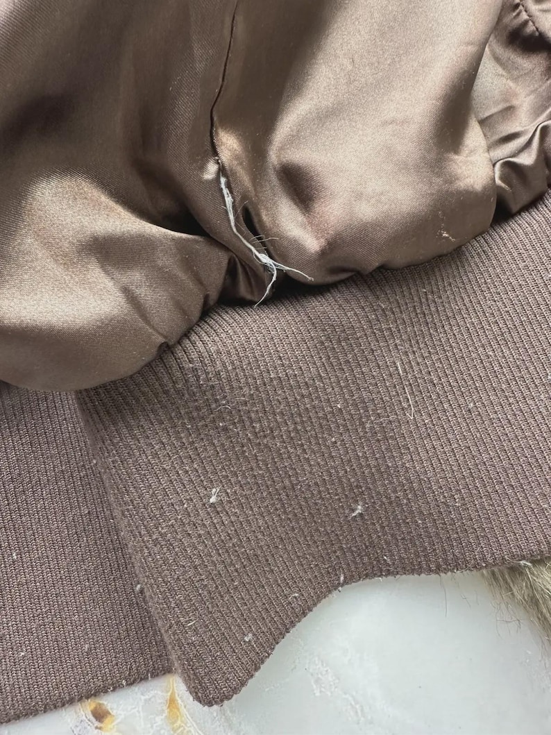 Puede incluir: Primer plano del forro de una chaqueta marr&oacute;n. El forro es de un material liso, similar al sat&eacute;n, y el pu&ntilde;o es de punto acanalado. La costura es visible donde el forro se encuentra con el pu&ntilde;o. La chaqueta parece usada.