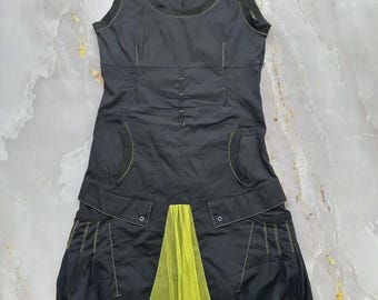 May include: A sleeveless black dress featuring lime green contrast stitching, a scoop neckline, and two front pockets. The lower section includes a lime green mesh panel and a ruffled hemline, with a gathered skirt design and silver-tone hardware.