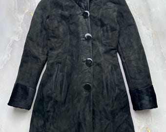 May include: A black suede coat with a high collar and fur trim on the collar and cuffs. The coat has a button-down front and a tailored fit. The coat is a mid-length style, suitable for cooler weather.