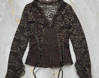May include: A long-sleeve top featuring dark brown floral lace on the sleeves and upper bodice, with a solid brown center panel. The garment includes a V-neckline with ruffles, corset-style ribbon lacing on the sides, and ruffled sleeve cuffs.