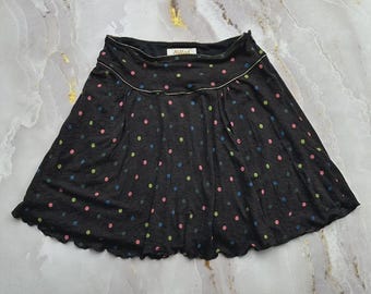 May include: A black mini skirt featuring a scattered polka dot pattern in shades of pink, blue, and green. The skirt has a wide waistband with a subtle metallic trim and a label inside that reads Killah. The hemline has a soft, wavy finish.