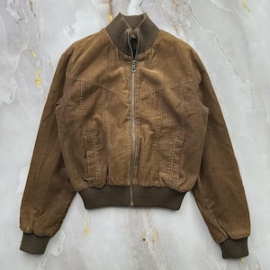May include: A brown corduroy bomber jacket featuring a full-length front zipper, a ribbed stand-up collar, ribbed cuffs, and a ribbed hem. The jacket includes two side pockets and decorative stitching across the chest area.