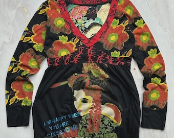 May include: A long-sleeve black tunic featuring a V-neckline with red trim, a floral pattern in red, orange, and green, and a graphic of a person with traditional hair styling. The text "I'M HAPPY WHEN YOU ARE CLOSE TO ME" is printed on the front.