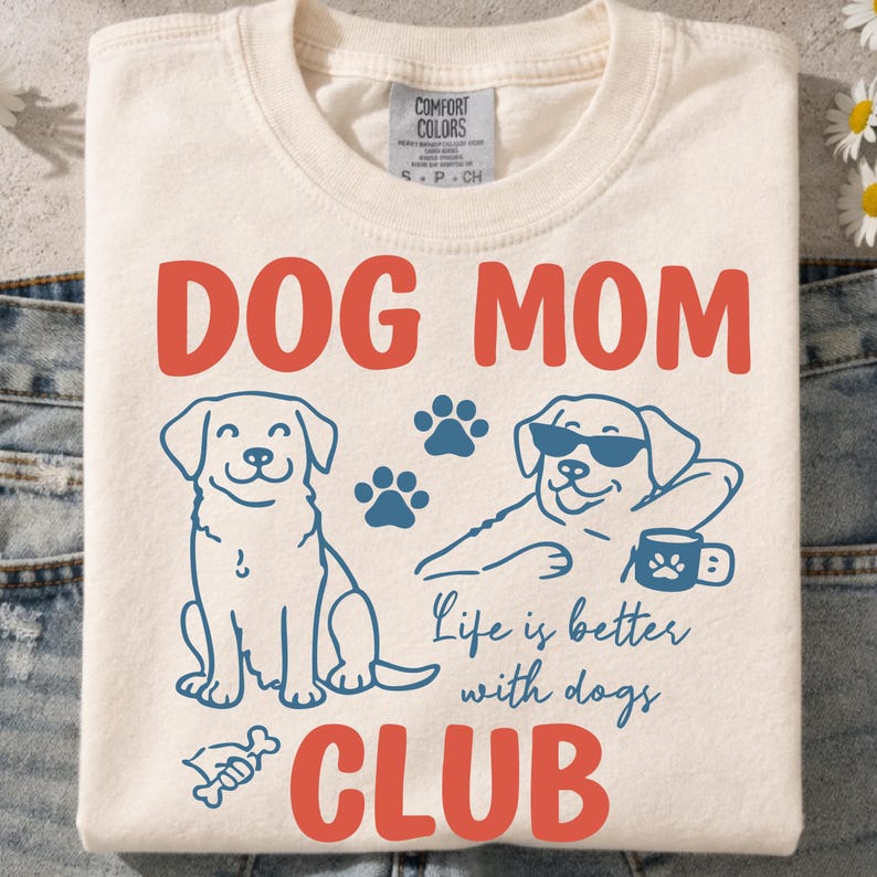 Dog Mom Club t-shirt mockup featuring cute dog illustrations, paw prints, and “Life is better with dogs” quote. Displayed on a folded cream shirt, perfect for dog moms, pet lovers, and gift ideas. Ideal for sublimation and print-on-demand.