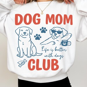 Model wearing a Dog Mom Club sweatshirt featuring cute dog illustrations, paw prints, and “Life is better with dogs” quote. Great for cozy outfits, pet lovers, and dog mom gifts.