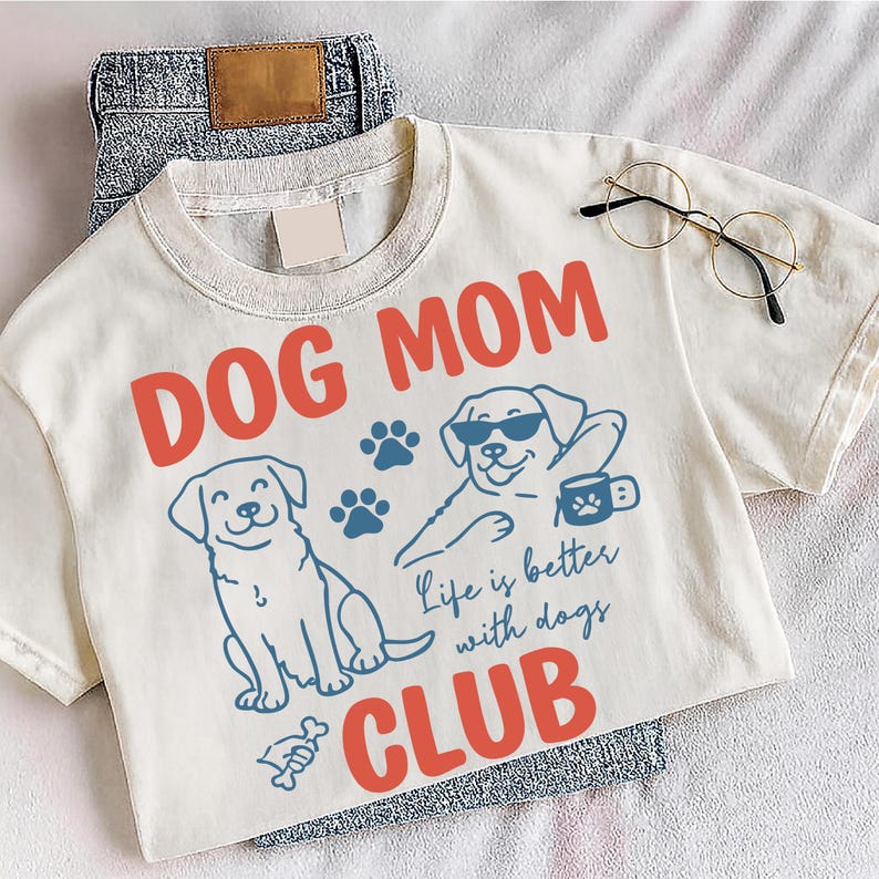 Dog Mom Club design displayed on a grey shirt outdoors with fun dog graphics and paw prints. Ideal for dog moms, animal lovers, and casual wear. Perfect for sublimation and print-on-demand designs.
