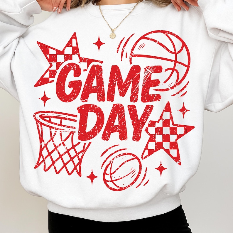 This ALT text describes a bright white oversized sweatshirt being worn by a woman, featuring a bold red “GAME DAY” basketball print covering the front. The distressed red lettering is surrounded by basketball sketches, sparkles, a hoop graphic, and checkered stars. The model’s pose highlights the full width of the design, showing how it spans from the upper chest to the waistline. This sweatshirt is perfect for basketball enthusiasts, sports moms, cheer teams, and spirited game-day outfits.