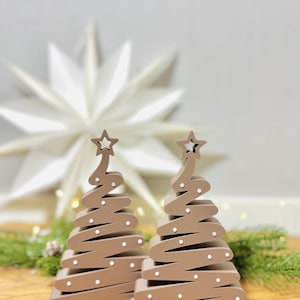 May include: Two brown wooden Christmas tree decorations with a star on top and white dot accents. The trees have a unique spiral design and are set on a wooden surface. Festive holiday decor.