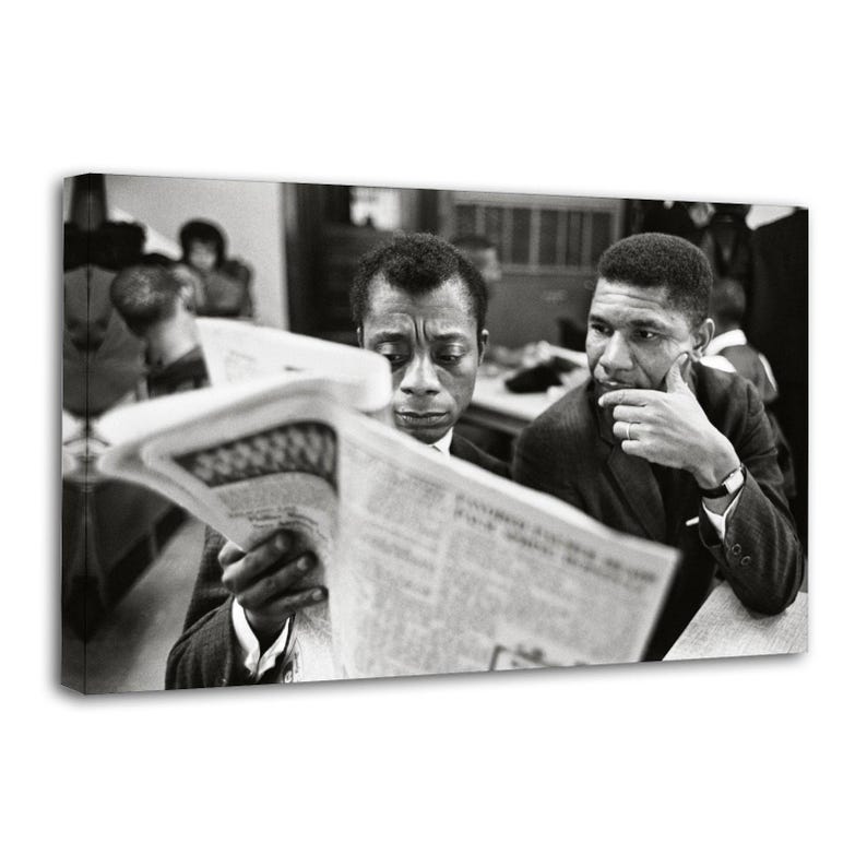 May include: Black and white photograph of two men, one reading a newspaper, the other looking on thoughtfully. The man reading is in a suit and tie, while the other man is wearing a suit. The image is a portrait, likely taken indoors.