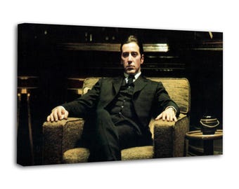 Op de afbeelding: Een canvas print met een man in een zwart pak die in een beige fauteuil zit. De man kijkt de kijker recht aan. Een kleine bijzettafel en lamp zijn zichtbaar op de achtergrond. De afbeelding heeft een donkere, dramatische uitstraling.
