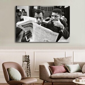 May include: Black and white framed print featuring two men reading a newspaper. One man is holding the newspaper, while the other is resting his chin on his hand. The print is displayed above a sofa and chair.