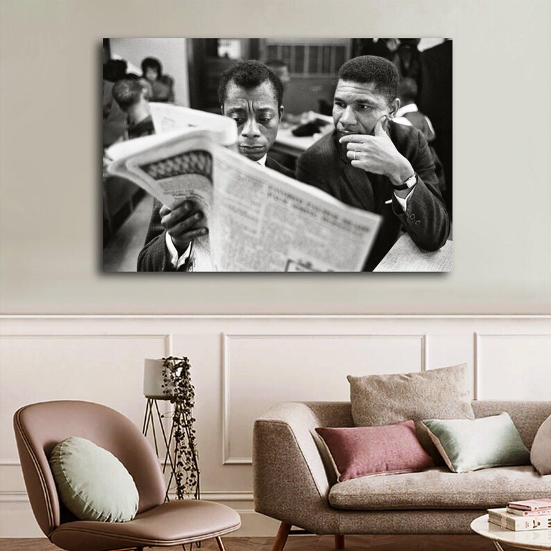 May include: Black and white framed print featuring two men reading a newspaper. One man is holding the newspaper, while the other is resting his chin on his hand. The print is displayed above a sofa and chair.