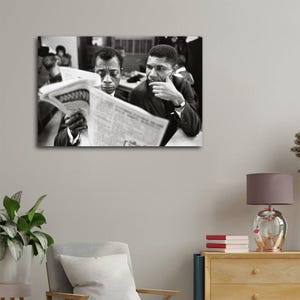 May include: Black and white photograph of two men reading a newspaper. One man is holding the newspaper, while the other is looking on with his hand on his chin. The image is a portrait, with the subjects in suits.