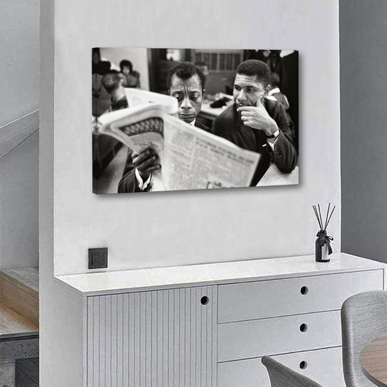 May include: Black and white framed print featuring two men reading a newspaper. One man is intently focused on the paper, while the other appears to be deep in thought. The print is displayed on a white wall.