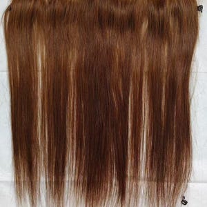 以下が含まれることがあります： 長くまっすぐな髪の毛束が付いた茶色のヘアピース。髪は暖かく赤みがかった茶色で、人毛のようです。ヘアピースはおそらくレースフロントまたは同様のタイプのヘアエクステンションです。