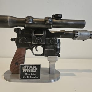 Peut inclure: Réplique du blaster DL-44 de Han Solo de Star Wars, avec une finition gris foncé et une poignée marron. Le blaster est monté sur un support gris, avec une plaque Star Wars indiquant "Han Solo DL-44 Blaster".