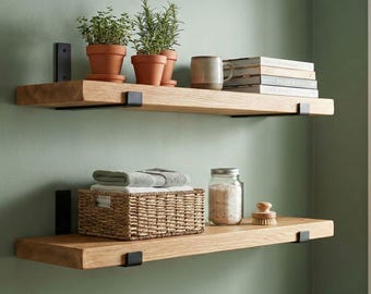 May include: Two wooden floating shelves with black metal brackets against a green wall. The top shelf holds potted herbs, a mug, and books. The bottom shelf features a woven basket, towels, a jar, and a brush.