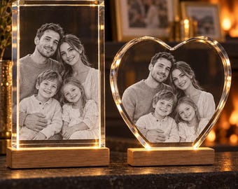 May include: Two illuminated glass photo displays featuring a family portrait. One is a rectangular block and the other is heart-shaped. Both are made of clear glass with laser-etched images, mounted on light-colored wooden bases with integrated LED lights.