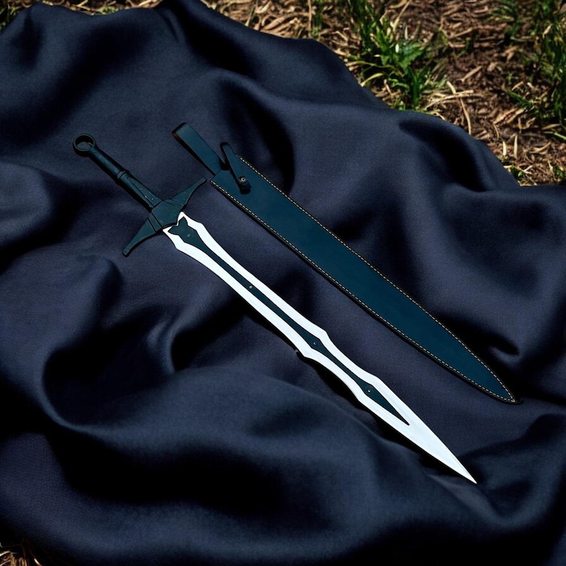 May include: A black and silver sword with a matching sheath rests on a dark blue fabric. The sword features a crossguard and a decorative design on the blade. The sheath is also black with a tan-colored stitch.