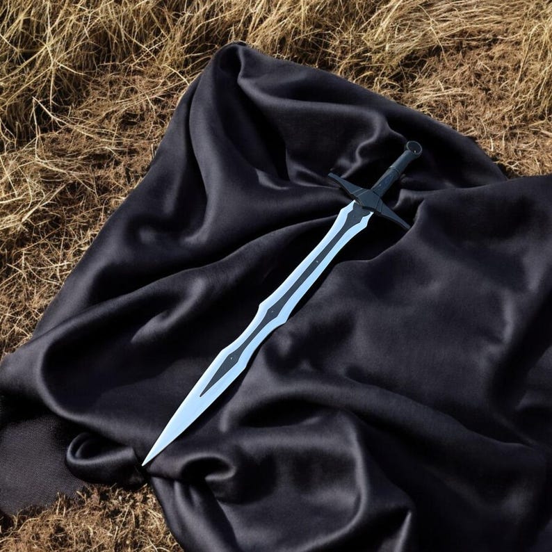 May include: A black and silver sword with a crossguard, resting on a black satin cloth. The blade has a light blue center and a decorative edge. The background is dry grass.