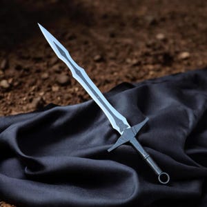 May include: A fantasy sword with a translucent blade and a black hilt. The blade has a decorative design along its length. The hilt features a crossguard and a ring at the pommel. The sword rests on a black cloth.