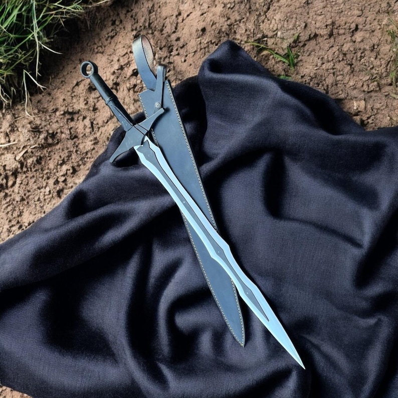 May include: A black sword with a silver blade rests in its black leather sheath on a black cloth. The sword has a cross-shaped hilt and a ring at the pommel. The blade has a decorative design.