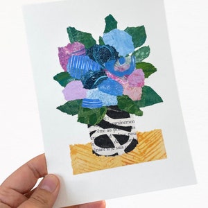 May include: A collage of paper flowers in a black and white striped vase. The flowers are blue, pink, and green. The vase is sitting on a yellow and orange background.