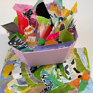 Peut inclure: Un bol rose clair rempli d'une variété de morceaux de papier déchirés aux couleurs vives, notamment vert, jaune, orange, rouge, noir et blanc. Les morceaux de papier présentent des textures, des motifs et du texte imprimé variés en collage.