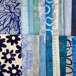May include: A collection of vertical paper strips in various shades of blue, featuring diverse patterns including dark blue floral prints, handwritten script, maps, botanical sketches, geometric circles, French text, and musical notation.