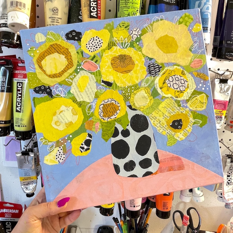 May include: A colorful floral painting featuring a bouquet of yellow flowers in a black and white polka-dotted vase. The flowers have textured petals and are set against a light blue background. A pink surface is below the vase.
