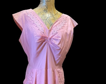May include: A pink sleeveless dress with a V-neckline and embroidered leaf details on the neckline and pockets.