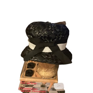 May include: A black hat with a textured pattern, a white band, and a black bow. The hat sits atop a wooden tray with black objects and a gold-wrapped item. The tray rests on a magazine with the text "Paris and Rouge".
