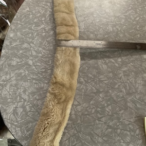 Könnte beinhalten: Ein langer, beiger Kunstpelzbesatz, der etwa 30 cm lang ist.