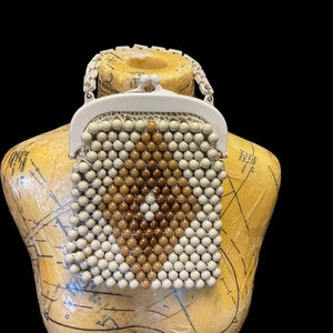 May include: A white beaded purse with a brown diamond pattern. The purse has a white plastic clasp and a white plastic chain strap.