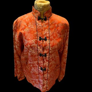 May include: A red and gold brocade jacket with black trim and frog closures. The jacket has a mandarin collar and long sleeves.