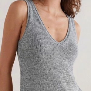 Puede incluir: Un top sin mangas de punto gris con cuello en V. La parte superior sin mangas está hecha de una tela de punto texturizada. El escote y las sisas están acabados con un ribete acanalado. La parte superior es de color neutro.