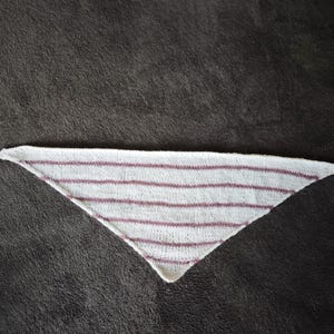 May include: A triangular knitted shawl featuring a white base color with horizontal stripes in a muted mauve or dusty rose color. The fabric has a visible knit texture throughout, and the garment is shaped into a wide point at the bottom center.