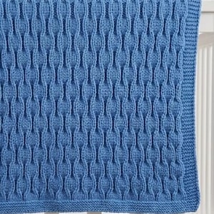 May include: A medium blue knitted blanket featuring a repeating vertical textured pattern of raised, rounded columns. The blanket has a simple garter stitch border along the edges, creating a uniform and consistent look across the entire surface.
