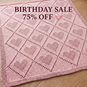 Può includere: Una coperta lavorata a maglia rosa chiaro con un motivo a rombi ripetuto e una forma a cuore testurizzata centrata all'interno di ogni rombo. Il testo BIRTHDAY SALE 75% OFF con una piccola icona a forma di cuore rosa è sovrapposto in alto.