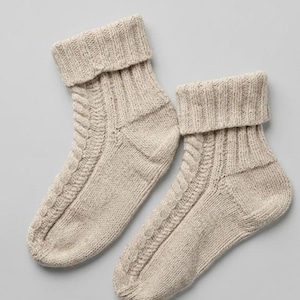 Peut inclure: Une paire de chaussettes en tricot beige avec un revers côtelé et un motif de torsades vertical sur le devant. Les chaussettes sont fabriquées dans un fil texturé au tissage visible, présentant un bord supérieur replié et un talon renforcé.