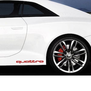 Pode incluir: Um carro branco com o emblema "quattro" vermelho na lateral. O carro tem um pneu preto com uma jante prateada e pinças de travão vermelhas. A carroçaria do carro é branca.