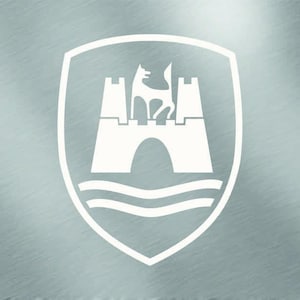 Pode incluir: Um emblema gráfico branco apresentando um castelo estilizado com duas torres e um arco central, encimado por uma figura de lobo em pé, tudo sobre duas linhas onduladas horizontais, num fundo de metal prateado escovado.