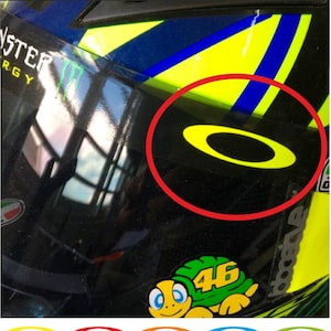 May include: Two oval-shaped stickers for a helmet visor, measuring 45mm x 15mm. The stickers are shown in a bright yellow color applied to a helmet visor, with a color chart below displaying various options including red, blue, and green.