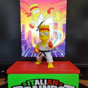 May include: A yellow Bart Simpson figurine in a karate uniform, with a red headband and gloves, stands on a red and green platform. The platform has the text "ITALIAN BRAINROT". A background image shows Bart in action with the text "BART-SAN!"