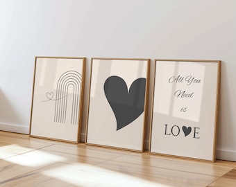 May include: Three framed art prints with gold-colored frames. The prints feature minimalist designs: a rainbow with a heart, a solid gray heart, and the text "All You Need is LOVE" with a heart symbol. The background is a light beige color.